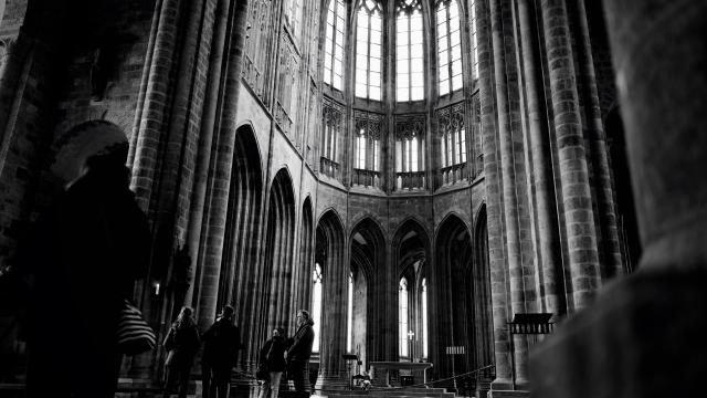 People walking in a Gothic cathedral with stained glass windows and towering pillars