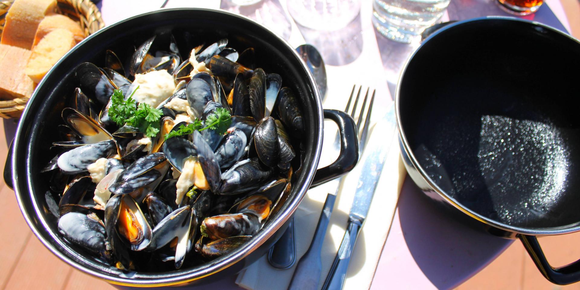 A pot of mussels marinières with open and closed shells, accompanied by parsley and bread