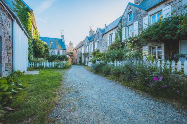 Cobblestone street lined with stone houses and well-maintained gardens