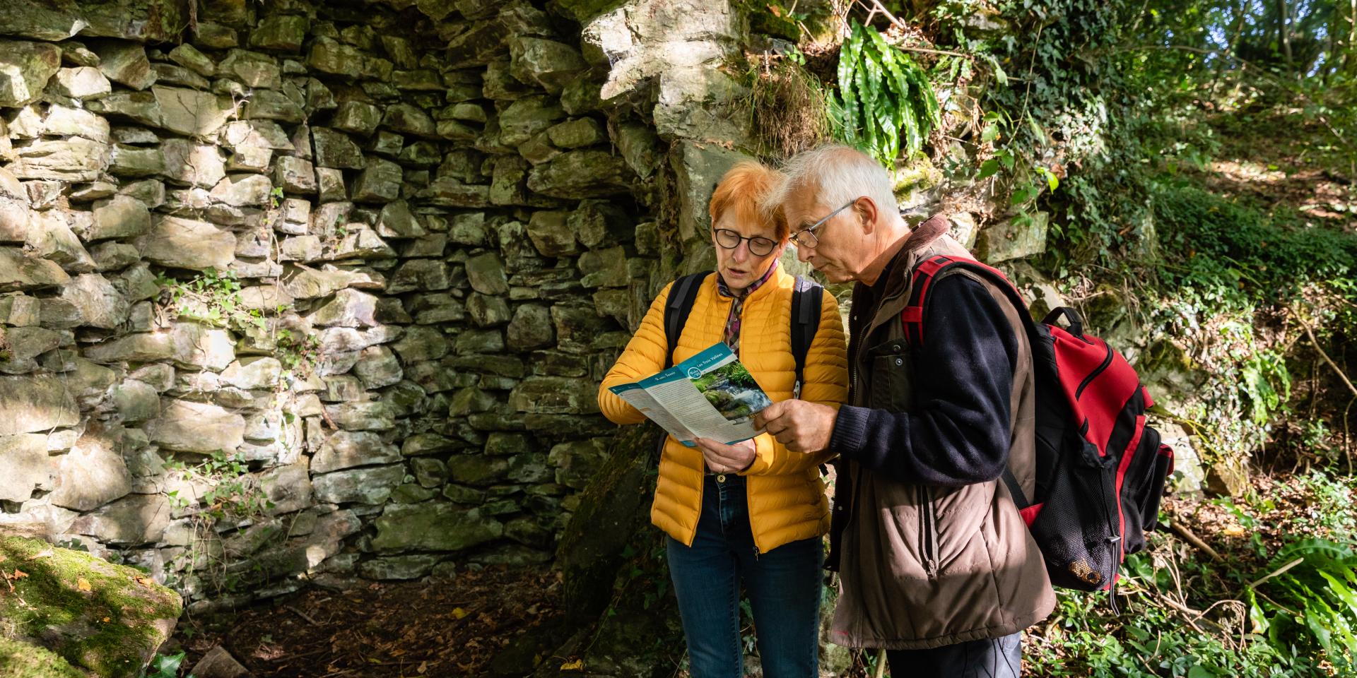 Two elderly people consulting a map near a stone wall in the countryside