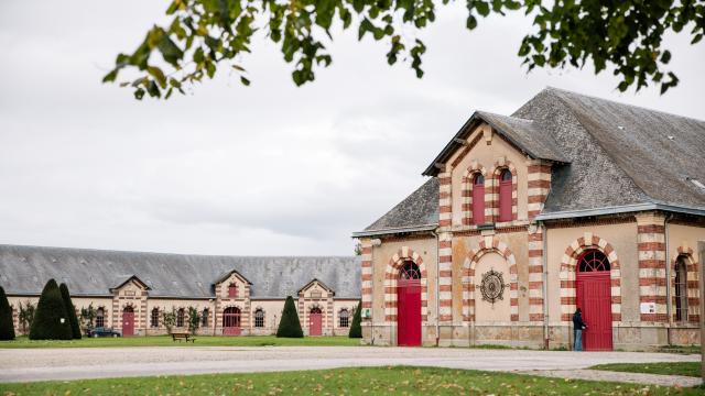 Red brick building with red doors and windows, surrounded by trees