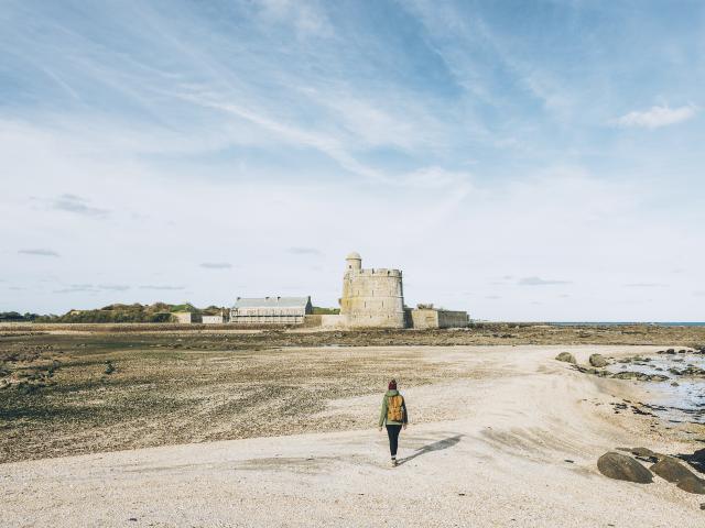 Person walking on a beach towards a stone castle