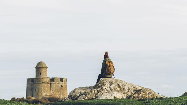 A traveler sitting on a rock facing a stone castle