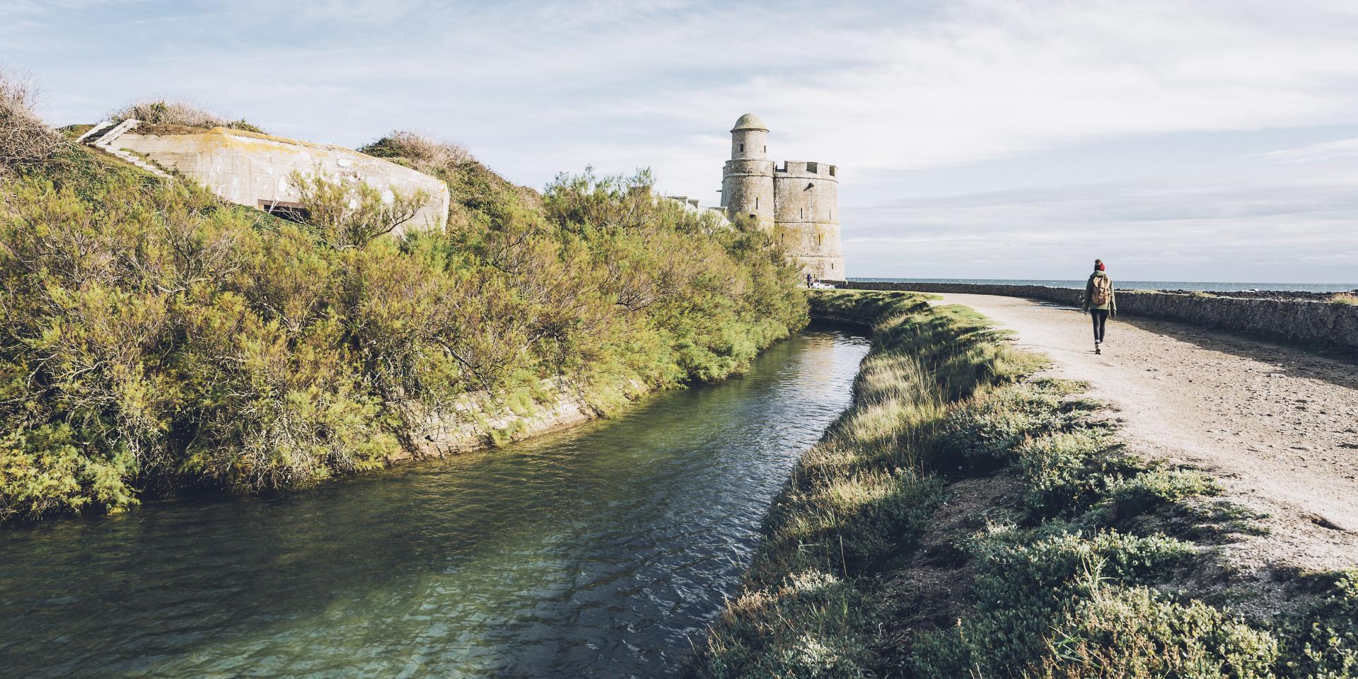 Person walking along a canal with a tower in the background