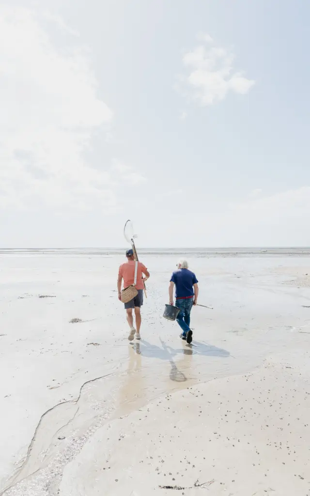Zwei Personen gehen an einem Sandstrand mit Schmetterlingsnetzen