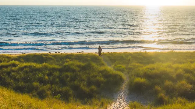 Person geht auf einem Sandweg zum Meer beim Sonnenuntergang
