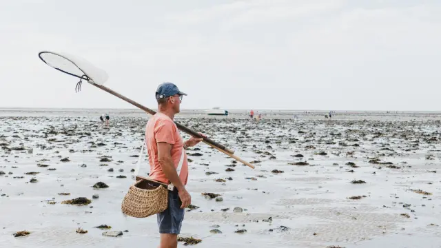 Un homme avec un filet à pêche sur une plage à marée basse à Agon Coutainville