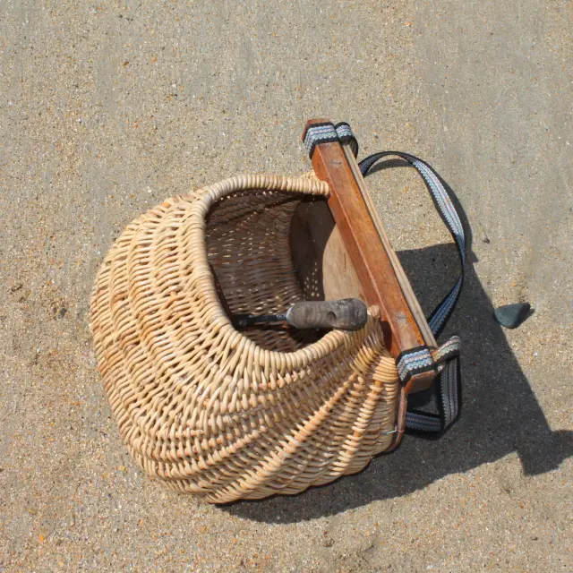 Ein Weidenkorb mit einem Holzgriff und einem schwarzen Gurt auf dem Sand