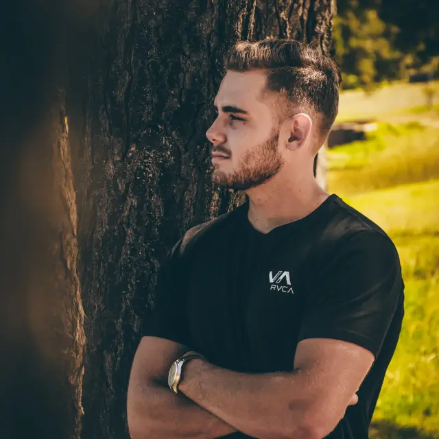 Un homme avec un t-shirt noir et une montre-bracelet, debout près d'un arbre