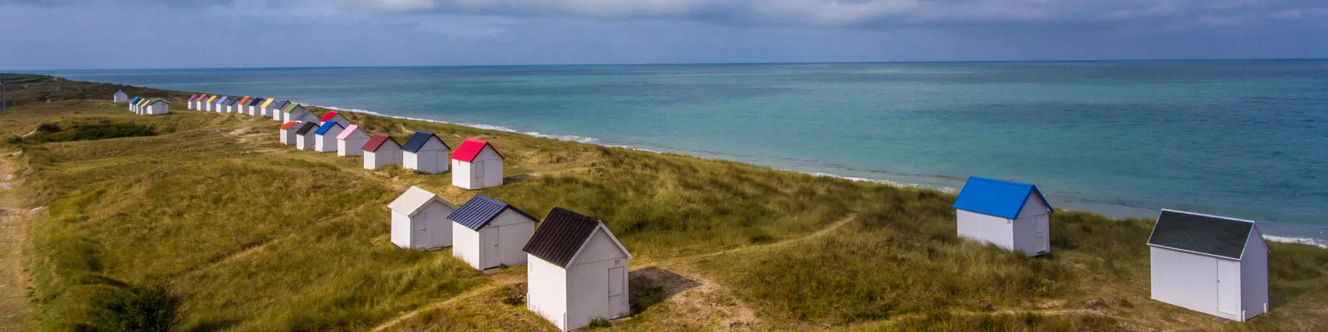 Eine Reihe bunter Strandhütten auf einem grasbewachsenen Hügel in der Nähe des Meeres
