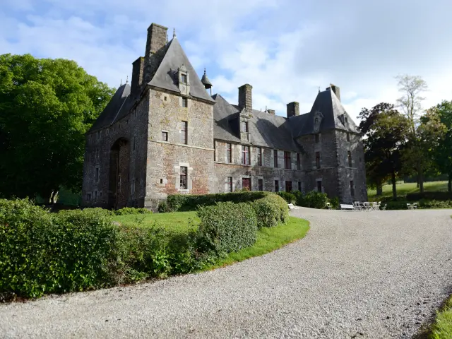 Château de Cerisy La Salle avec des toits pointus et des cheminées, entouré de buissons et d'arbres