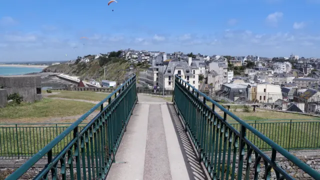 Un pont vert menant à Granville avec des maisons et un ciel bleu