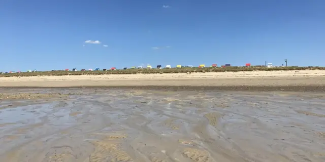 Sandstrand mit Fußabdrücken und flachem Wasser