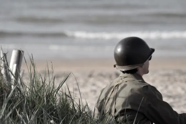 A soldier in military uniform gazes at the sea