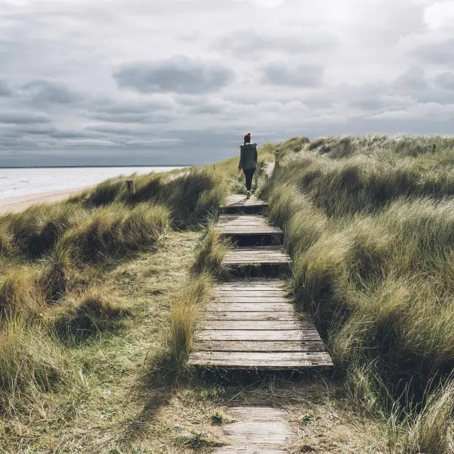 Person walking on a wooden path towards the sea
