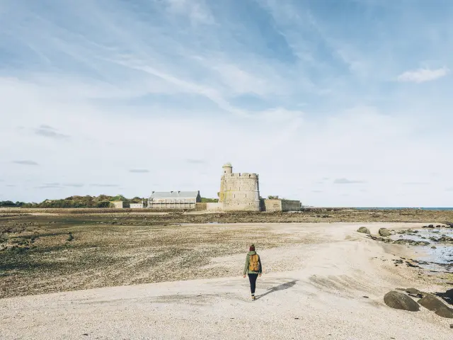Person geht am Strand auf ein Steinschloss zu
