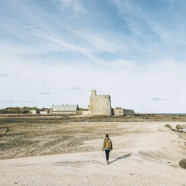 Person geht am Strand auf ein Steinschloss zu