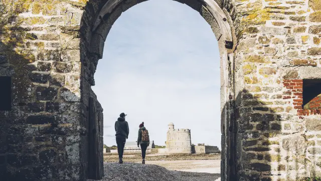 Zwei Personen gehen durch einen verfallenen Bogen zu einem entfernten Turm