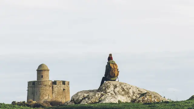 Ein Reisender sitzt auf einem Felsen gegenüber einem Steinschloss