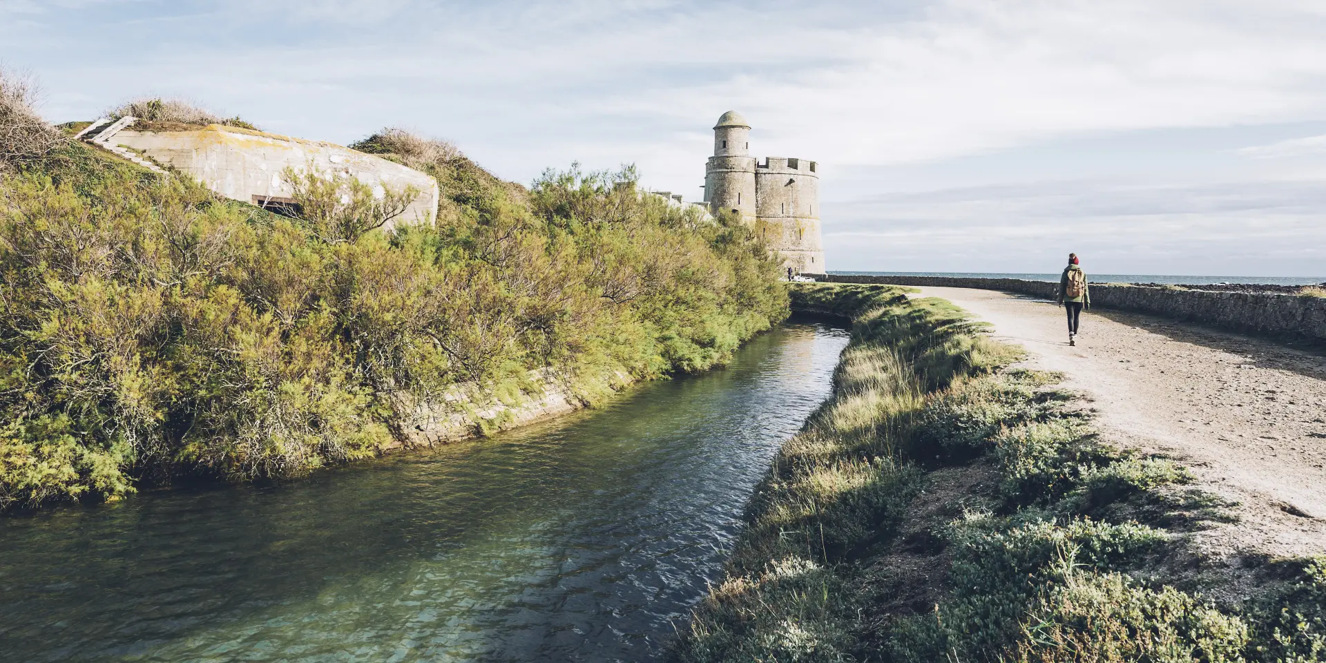 Person geht entlang eines Kanals mit einem Turm im Hintergrund
