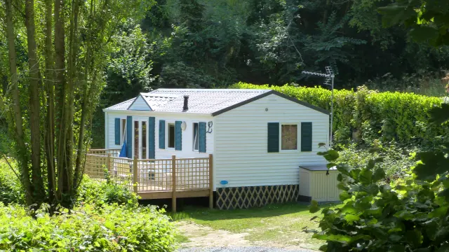 White mobile home with wooden deck and surrounding vegetation