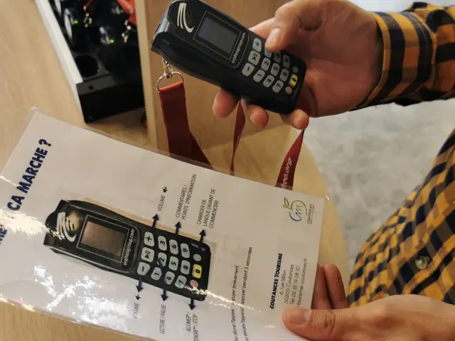 Une personne tient un audio-guide et une notice d'utilisation