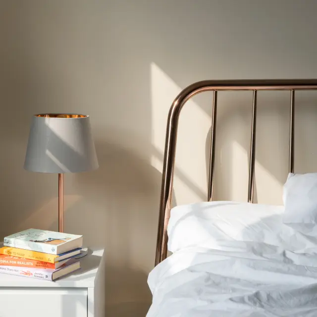 Bett mit einem Metallbettkopf und einer Nachttischlampe neben einem Stapel Bücher