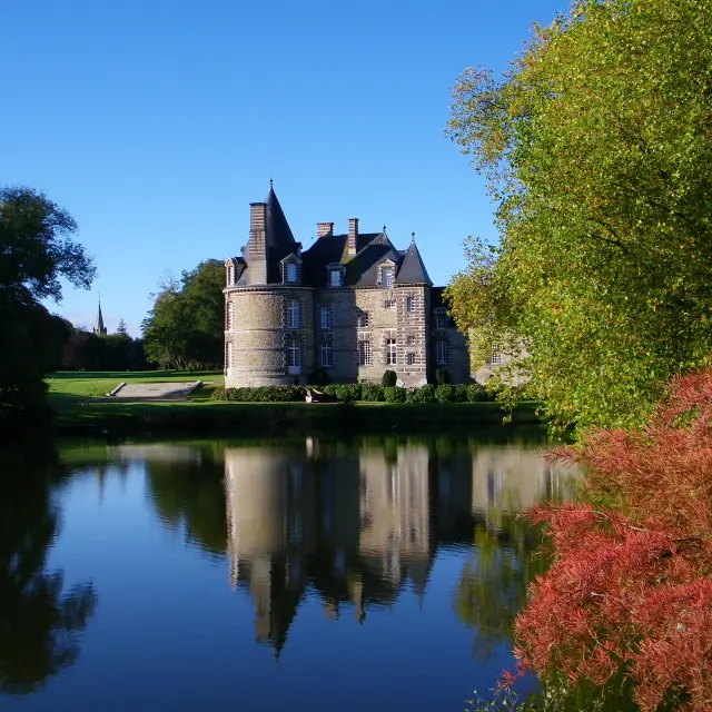 Ein Schloss umgeben von Bäumen und im Teich reflektiert
