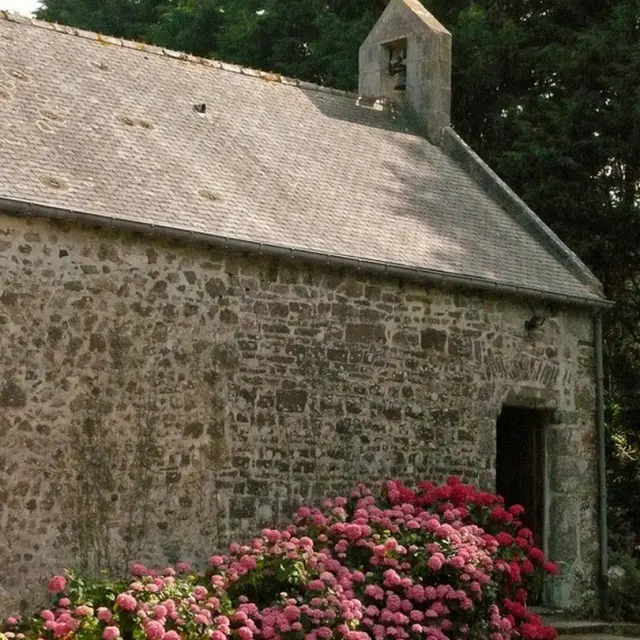 Steinkapelle mit rosa Blumen im Vordergrund