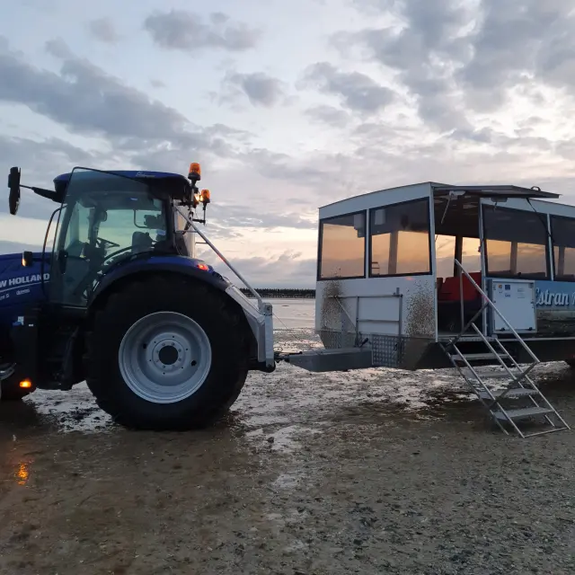Un tracteur bleu et un bateau blanc sur une plage au coucher du soleil : La Balade d'Anton