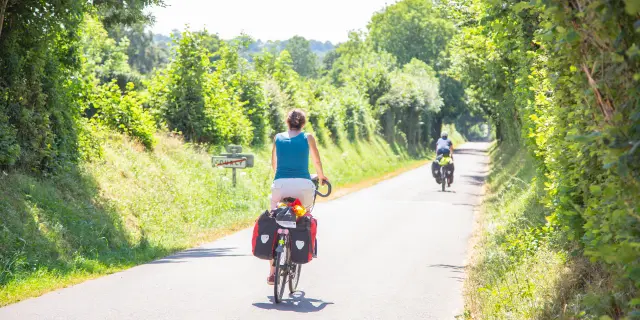 Deux cyclistes roulant sur une route de campagne bordée d'arbres et de végétation dans le bocage