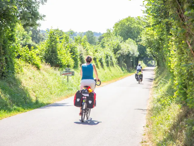 Deux cyclistes roulant sur une route de campagne bordée d'arbres et de végétation dans le bocage