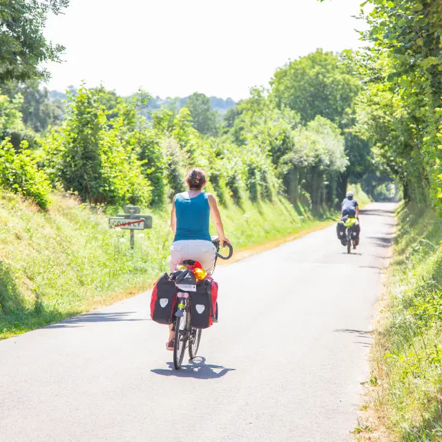 Deux cyclistes roulant sur une route de campagne bordée d'arbres et de végétation dans le bocage