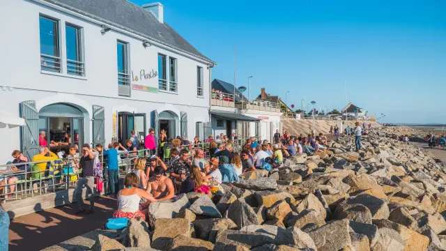 Crowded terraces in front of a white building with people sitting on rocks