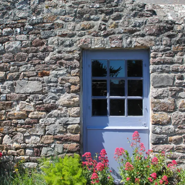 Porte en bois bleue avec des fleurs rouges et vertes à côté à Regnéville sur Mer