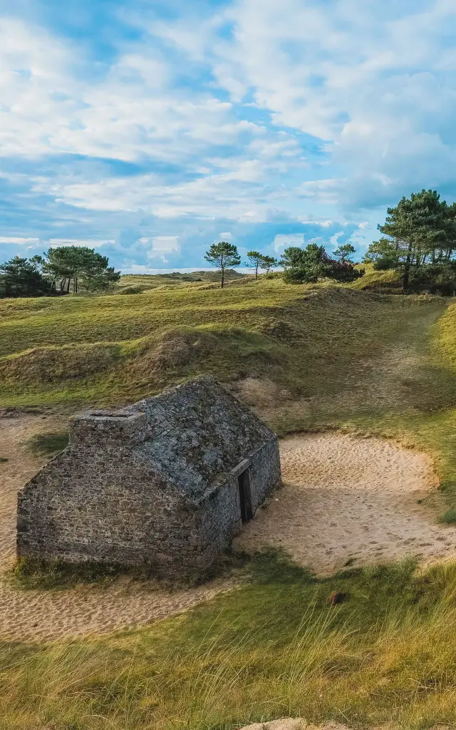Stone bunker surrounded by grassy dunes and a few trees