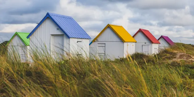 Colorful beach huts lined up on a grassy dune