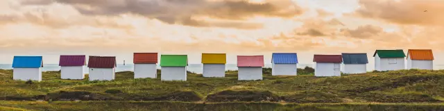 A row of colorful beach huts on a grassy hill at sunset