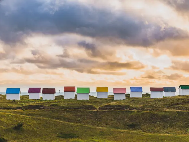 Eine Reihe bunter Strandhütten auf einem grasbewachsenen Hügel beim Sonnenuntergang