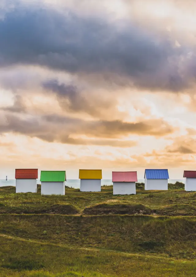 Eine Reihe bunter Strandhütten auf einem grasbewachsenen Hügel beim Sonnenuntergang