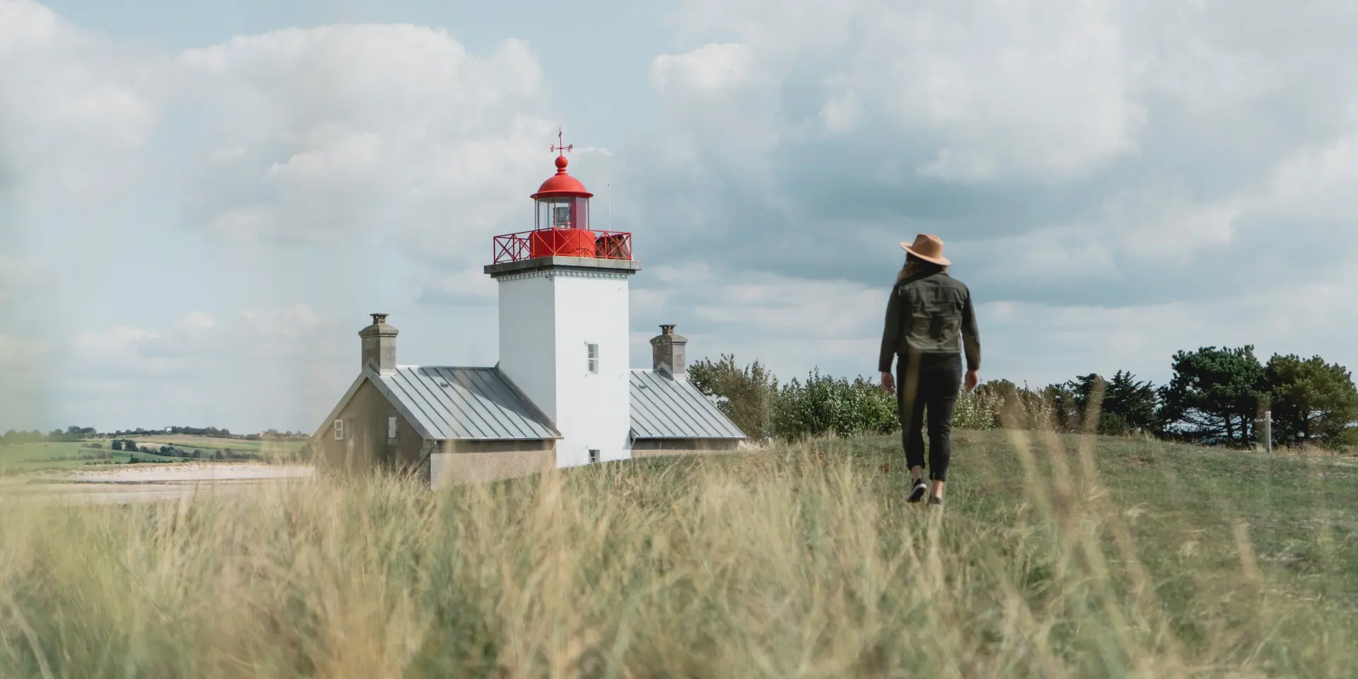 Person geht auf einen Leuchtturm in einem Feld mit hohem Gras zu