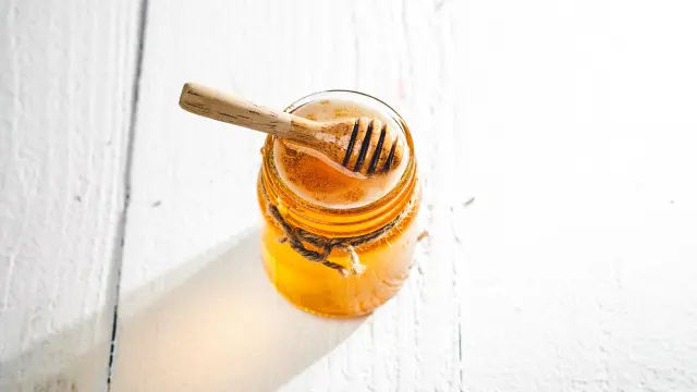 Un pot de miel transparent avec une cuillère en bois à l'intérieur