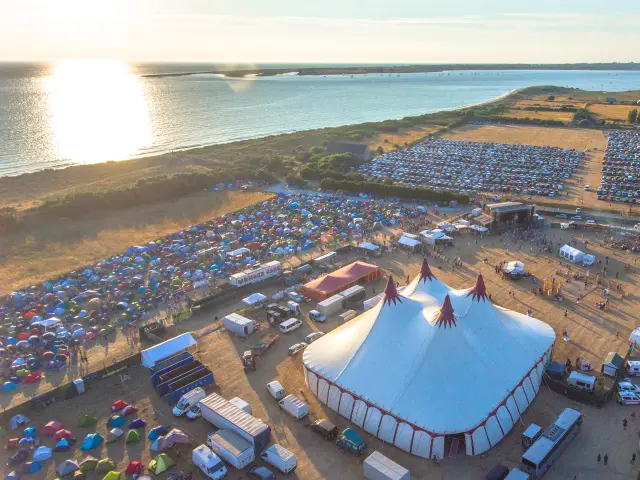 Luftaufnahme eines Festivals am Meer mit Zelten und Fahrzeugen