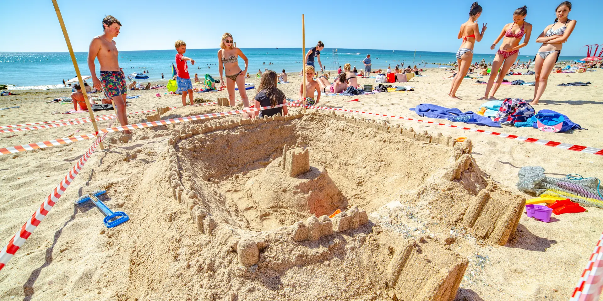 Eine große Sandburg umgeben von Menschen an einem sonnigen Strand