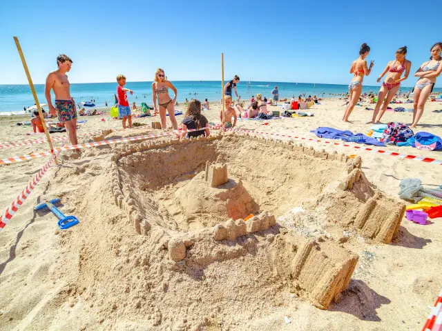 Eine große Sandburg umgeben von Menschen an einem sonnigen Strand