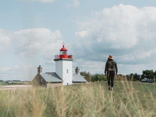 Person walking towards a lighthouse in a field of tall grass