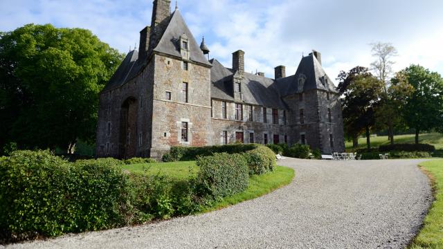 Château de Cerisy La Salle avec des toits pointus et des cheminées, entouré de buissons et d'arbres
