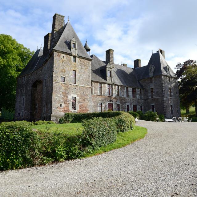 Château de Cerisy La Salle avec des toits pointus et des cheminées, entouré de buissons et d'arbres