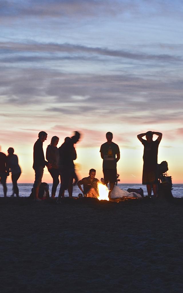 Un groupe de personnes autour d'un feu de camp sur une plage au coucher du soleil