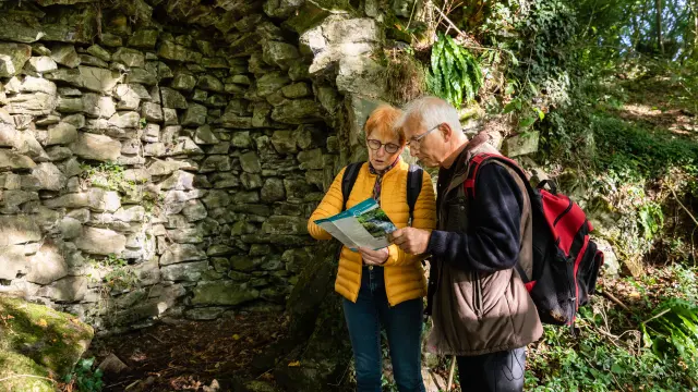 Two elderly people consulting a map near a stone wall